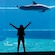 A girl standing with outstretched arms in front of a large aquarium exhibit with 2 dolphins swimming inside